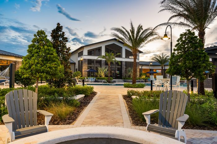 Luxurious apartment complex featuring a beautifully landscaped courtyard with palm trees, stylish seating areas, and a pristine swimming pool under a vibrant evening sky.