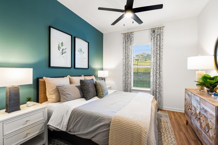 Inviting bedroom with a calming green accent wall, cozy bedding, and elegant decor, featuring abundant natural light through a large window.