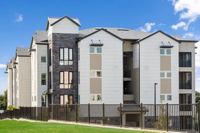 Modern apartment building with sleek architecture and vibrant exterior, nestled in a lush green setting under a clear blue sky.