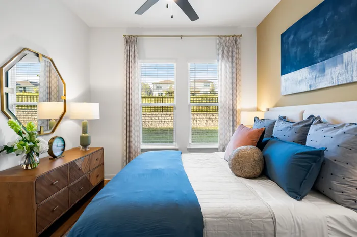 Bright and inviting bedroom featuring elegant decor, a comfortable bed with blue and orange pillows, and large windows letting in natural light.