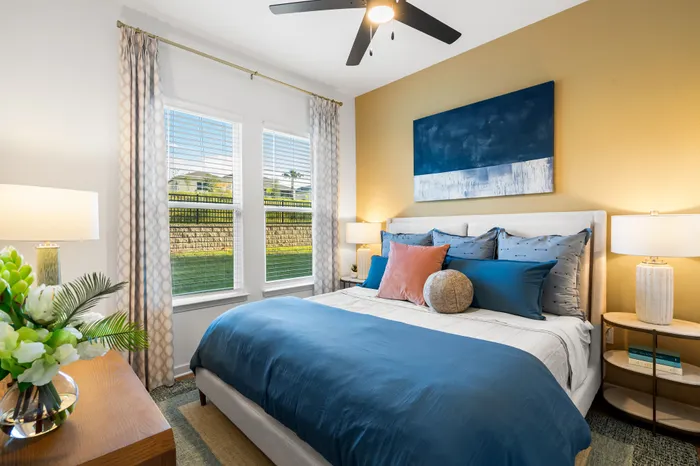 Inviting bedroom with blue and orange accents, modern artwork, and abundant natural light from large windows.