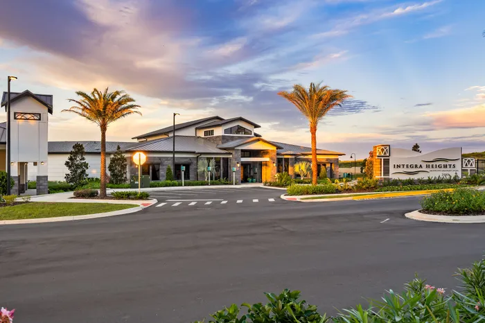 Elegantly designed building exterior of Integra Heights at sunset, surrounded by lush landscaping and palm trees, showcasing modern architecture and vibrant community living.