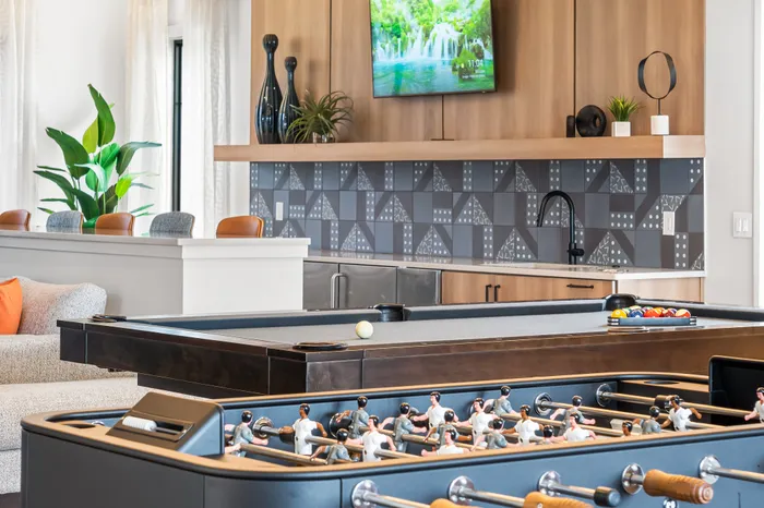 Modern recreational space featuring a sleek pool table and foosball game, with a stylish kitchenette and vibrant decor.