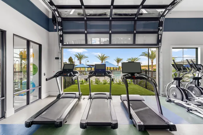 Modern fitness center with treadmills facing a scenic outdoor view, including palm trees and pool area, creating an inspiring workout environment.