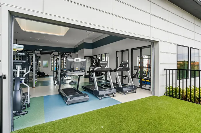 Modern fitness center with state-of-the-art gym equipment and vibrant interior design, opening to an outdoor green space.