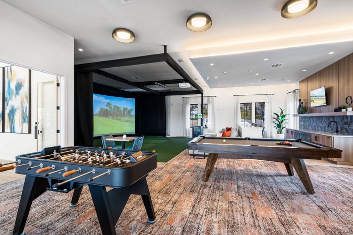 Luxurious recreation room featuring a sleek foosball table, elegant pool table, and a modern golf simulator for entertainment and relaxation.