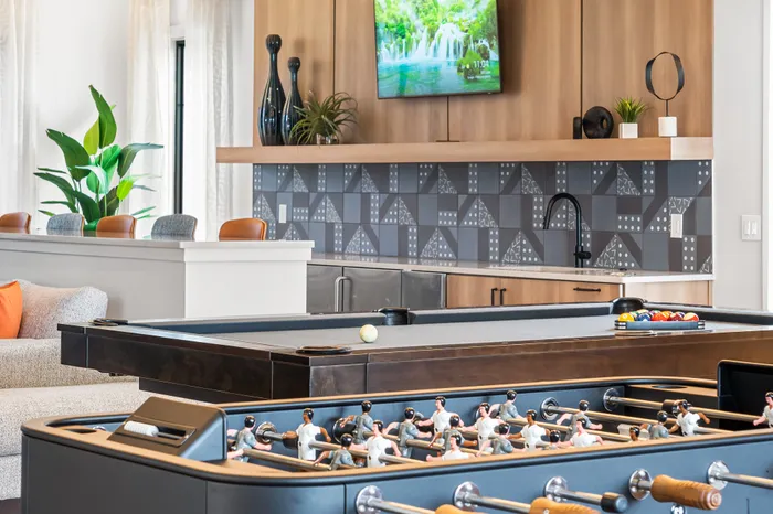 Sleek and modern entertainment room with a stylish pool table, foosball table, and a sophisticated bar area adorned with elegant decor.