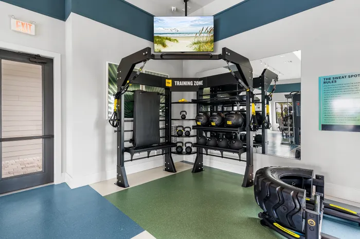 Modern gym with a well-equipped training zone featuring TRX equipment, kettlebells, and a flat bench, creating an inviting space for fitness enthusiasts.