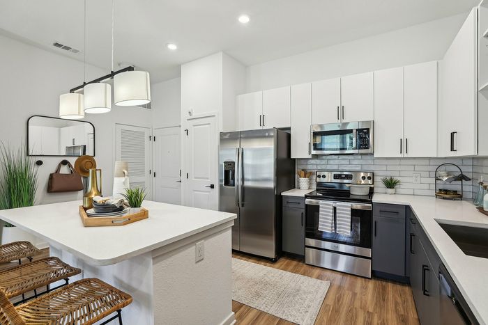 Modern kitchen with sleek stainless steel appliances, elegant cabinetry, and a stylish island with wicker bar stools, perfect for entertaining.