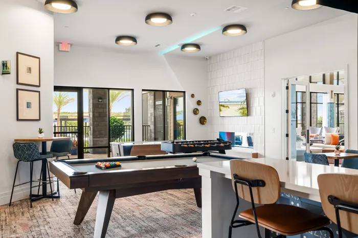 Elegant recreation area featuring a pool table and foosball alongside chic seating, large windows open to a sunlit patio.