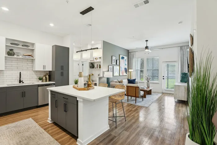 Inviting open-plan living area with modern kitchen, island seating, and cozy living room overlooking lush greenery.
