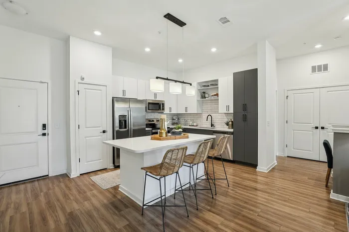 Modern kitchen with sleek cabinetry and a central island, featuring wooden flooring and stylish bar stools, offering a welcoming and open atmosphere.