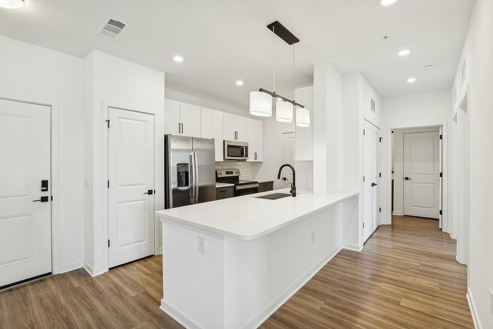 Modern kitchen with sleek stainless steel appliances, elegant pendant lighting, and a spacious white countertop island. Bright and inviting with beautiful wood flooring.