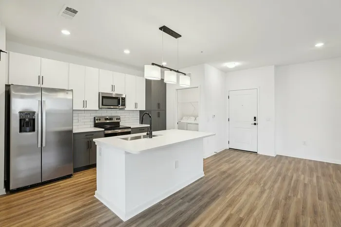 Modern kitchen with sleek stainless steel appliances, elegant white cabinetry, a stylish pendant light, and warm wood flooring.
