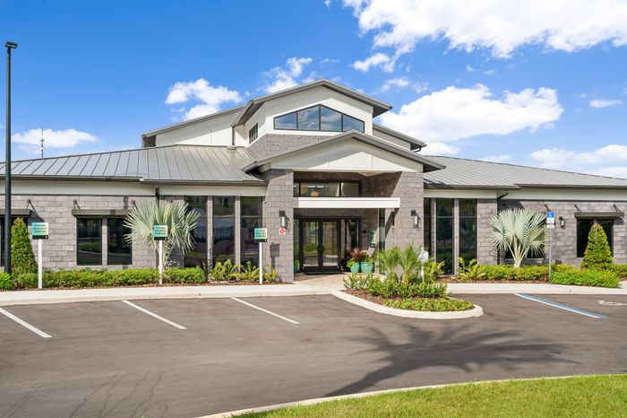Inviting apartment complex facade with modern architecture, lush landscaping, and ample parking under a clear blue sky.