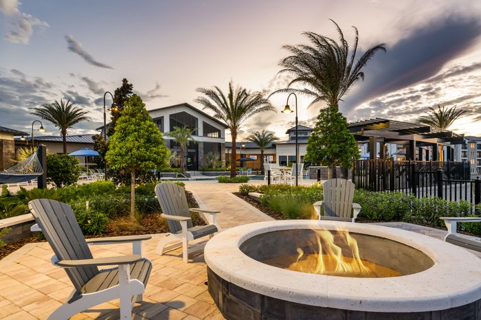 Luxurious outdoor community space featuring a cozy fire pit, elegant seating, and lush palm trees under a stunning sunset sky.