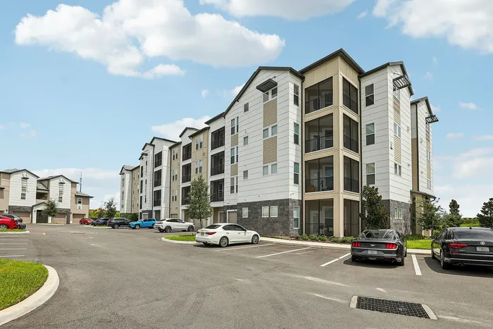 Modern multi-story apartment building with stylish balconies, ample parking, and lush surroundings under a clear blue sky.