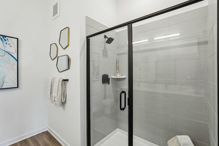 Modern bathroom with elegant glass shower enclosure, geometric mirrors, and stylish art adding a touch of sophistication.