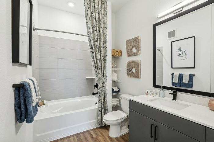 Modern bathroom design featuring elegant wood flooring, a chic vanity with a large mirror, stylish shelving with decor, and a cozy tub with a patterned curtain.