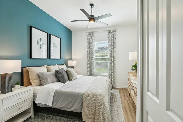 Elegant bedroom with chic teal accent wall, cozy bedding, and natural light streaming through stylishly curtained windows.