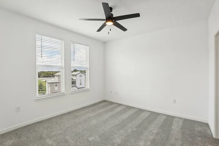 Bright, airy bedroom with plush carpet, large windows offering scenic views, and a modern ceiling fan, perfect for comfortable living.