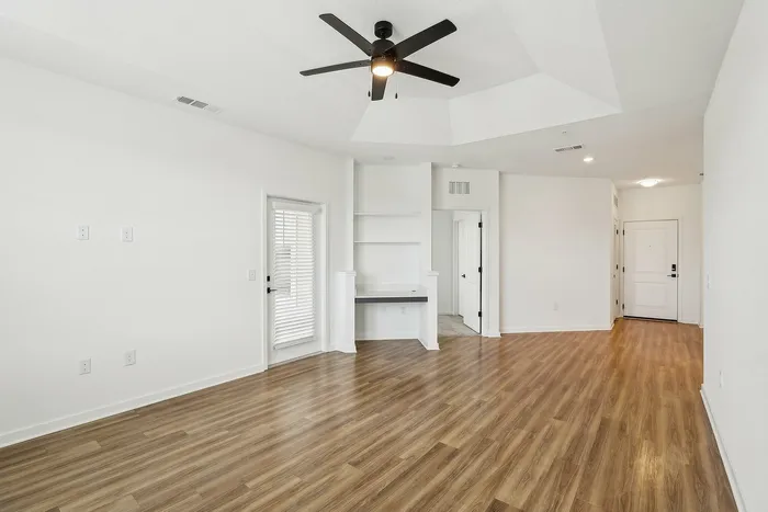 Spacious and elegant living area with modern ceiling fan, hardwood floors, and abundant natural light, perfect for a cozy yet stylish home.