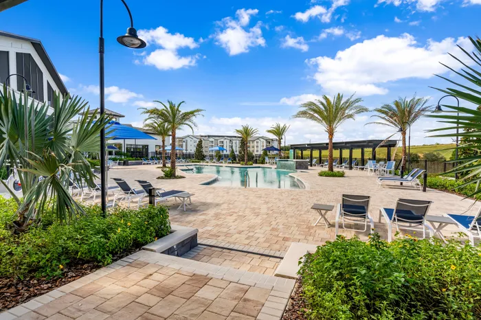 Luxurious apartment complex featuring a stunning outdoor pool area surrounded by palm trees and sun loungers, perfect for relaxation under a bright blue sky.