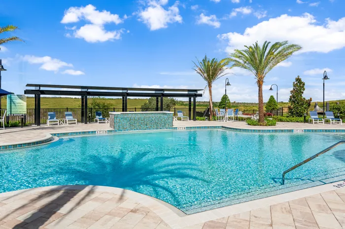 Luxurious outdoor pool area with crystal-clear water, elegant lounge chairs, and stunning palm trees under a bright blue sky.