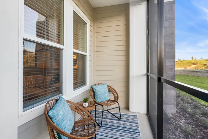 Charming sunlit balcony with cozy wicker chairs, bright blue cushions, and a small plant table, perfect for relaxation and enjoying the scenic view.