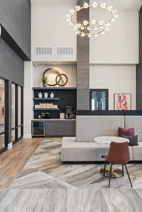 Elegant communal lounge with modern decor, featuring a stylish chandelier, plush seating, and a sophisticated kitchenette with open shelving.