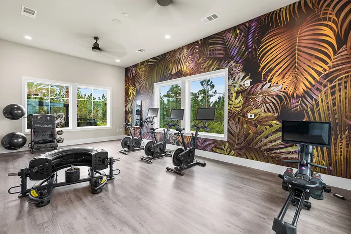 Vibrant home gym with modern exercise equipment, tropical-themed wall design, and large windows for natural light.