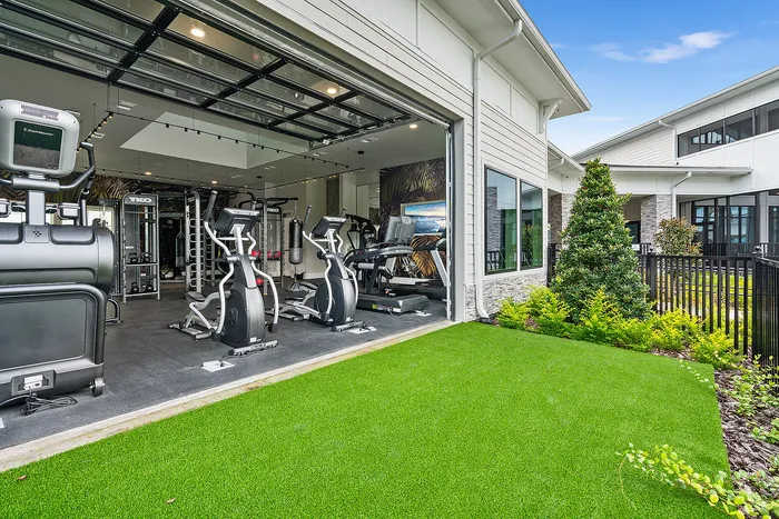 Modern gym with state-of-the-art fitness equipment, featuring large windows and lush outdoor greenery for a refreshing workout environment.