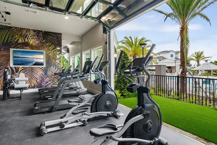 Modern fitness center with state-of-the-art equipment, tropical wall art, and open views of a luxurious pool area, ideal for a vibrant lifestyle.