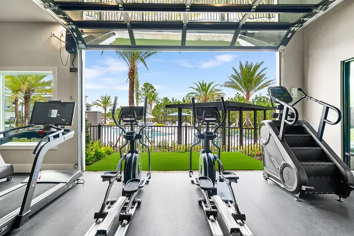 Modern fitness room with state-of-the-art exercise equipment and a scenic view of palm trees and a pool area.