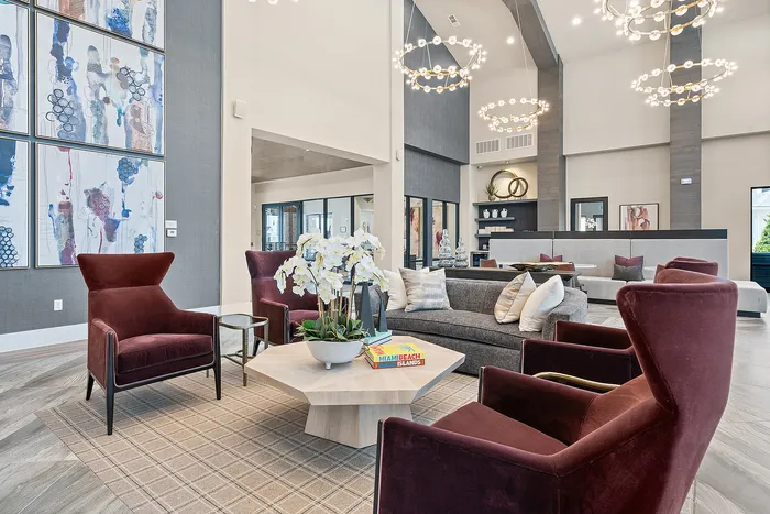 Elegant community lounge featuring plush burgundy chairs, a stylish gray sofa, and chic art deco chandeliers, creating a sophisticated and inviting atmosphere.