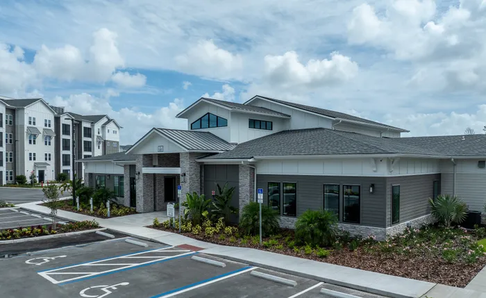 Modern apartment complex with stylish architecture, beautifully landscaped gardens, and ample parking under a clear blue sky.