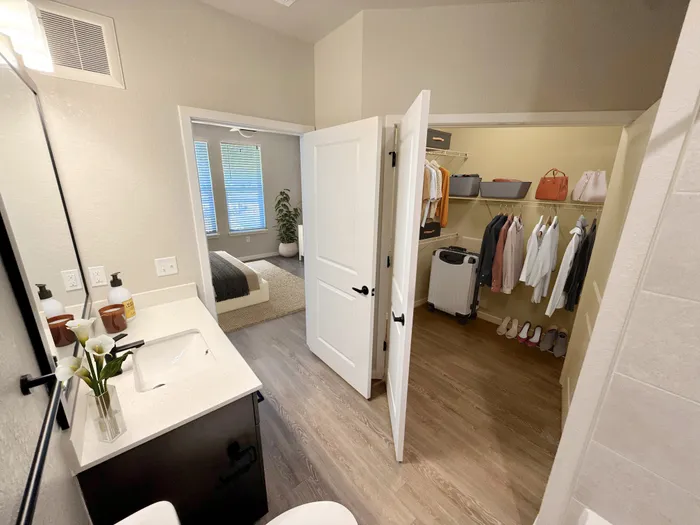 Elegant apartment showcasing a modern bathroom, spacious walk-in closet with organized shelving, and view into a serene bedroom with large windows.