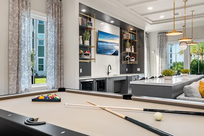 Modern, sunlit living space featuring a sleek billiards table, stylish bar area with shelving, and elegant hanging lights, perfect for entertaining.