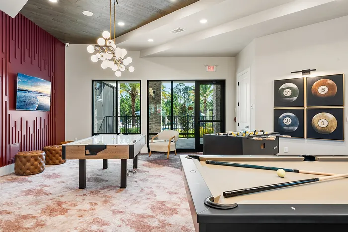 Luxurious apartment game room featuring a pool table, stylish decor, and vibrant artwork, with large windows offering natural light and lush views.