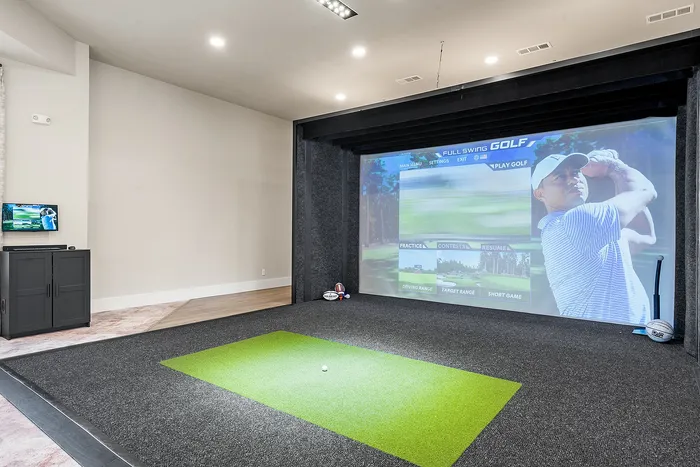 Luxurious indoor golf simulator room with state-of-the-art equipment and a vibrant screen, perfect for golfing enthusiasts.