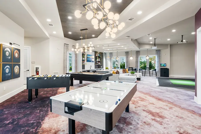Luxurious entertainment room with modern air hockey, foosball tables, and elegant seating area under stylish lighting fixtures.