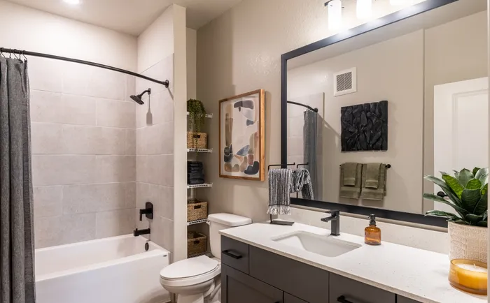 Modern bathroom featuring a spacious bathtub, sleek vanity with a large mirror, and stylish decor including a plant and abstract art.