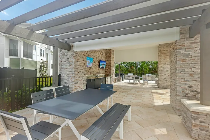 Elegant outdoor patio with modern dining set under a wooden pergola, featuring stylish stone walls, charming seating, and serene garden views.