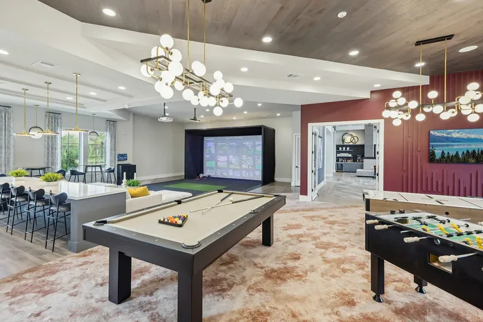 Luxurious recreational room with pool table, foosball, modern lighting, and a virtual golf setup, perfect for entertainment and relaxation.