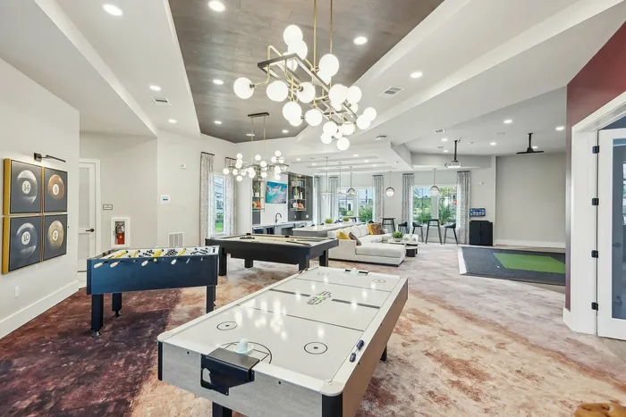 Elegant recreation room showcasing modern lighting, plush seating area, and exciting game tables including foosball, pool, and air hockey.