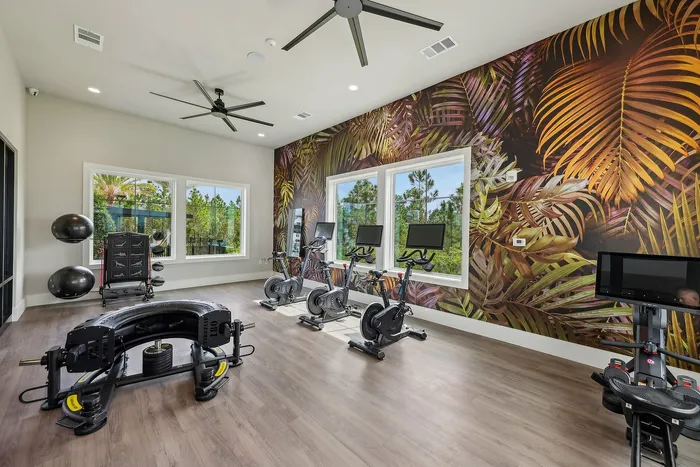 Modern fitness room with sleek exercise bikes, vibrant tropical wallpaper, and large windows offering a scenic outdoor view.