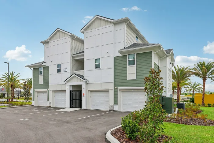 Modern multi-story residential building with green and white exterior, surrounded by lush landscaping and palm trees, under a clear blue sky.