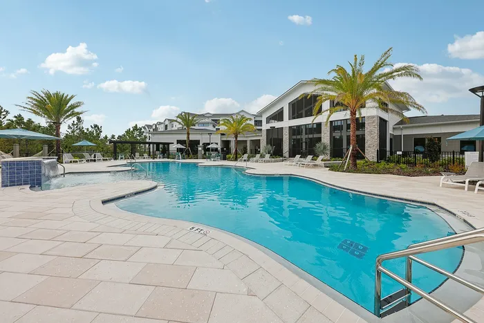 Luxurious apartment complex with a resort-style pool and palm tree-lined surroundings, perfect for relaxation under a clear blue sky.