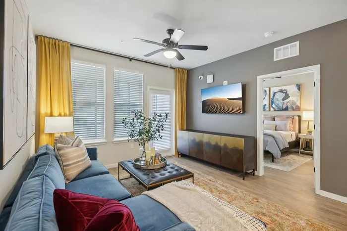 Inviting living room with a plush blue sofa, vibrant yellow curtains, and stylish decor, seamlessly leading to a cozy bedroom.