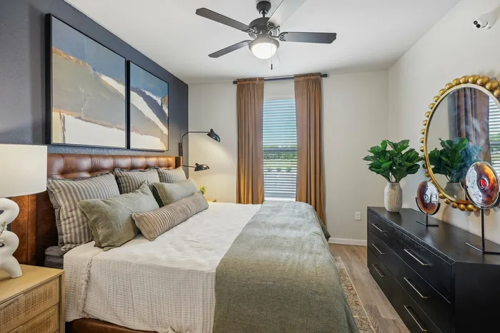 Elegant bedroom featuring a plush king-size bed with stylish pillows, modern artwork, and warm lighting, complemented by a chic dresser and large decorative mirror.